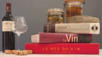 Trois livres sur le vin et la gastronomie mis en scène avec une bouteille de vin, un verre et des bocaux.